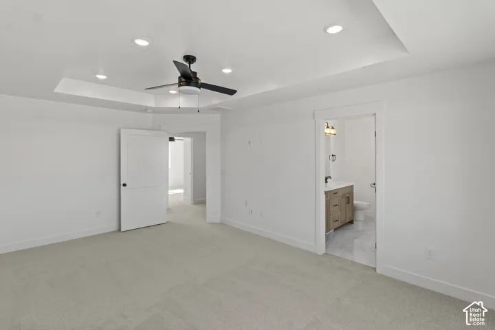 Tray ceiling with recessed lighting and a ceiling fan, light-toned carpeting, and a doorway leading to a space featuring a vanity with a dark countertop and a white toilet