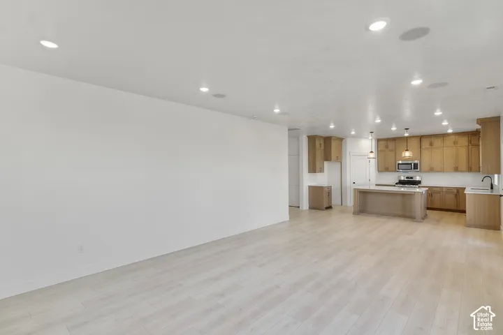Open-concept living area featuring light wood-finish flooring, recessed lighting, and a kitchen with warm-toned cabinetry, a central island, and stainless steel appliances