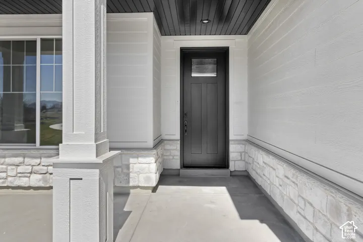 Front entry featuring a dark-paneled door with an integrated glass panel, white siding, and a stone-clad foundation
