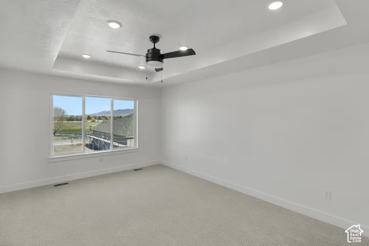 Recessed lighting illuminating a tray ceiling, ceiling fan with light kit, large picture window, and neutral carpet flooring