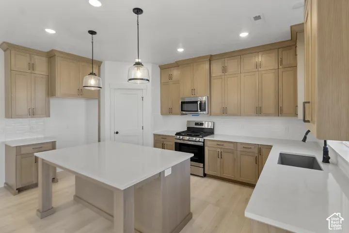 Kitchen featuring wood-finish cabinetry, stainless steel appliances, a center island with a light-toned countertop, recessed lighting, and pendant fixtures