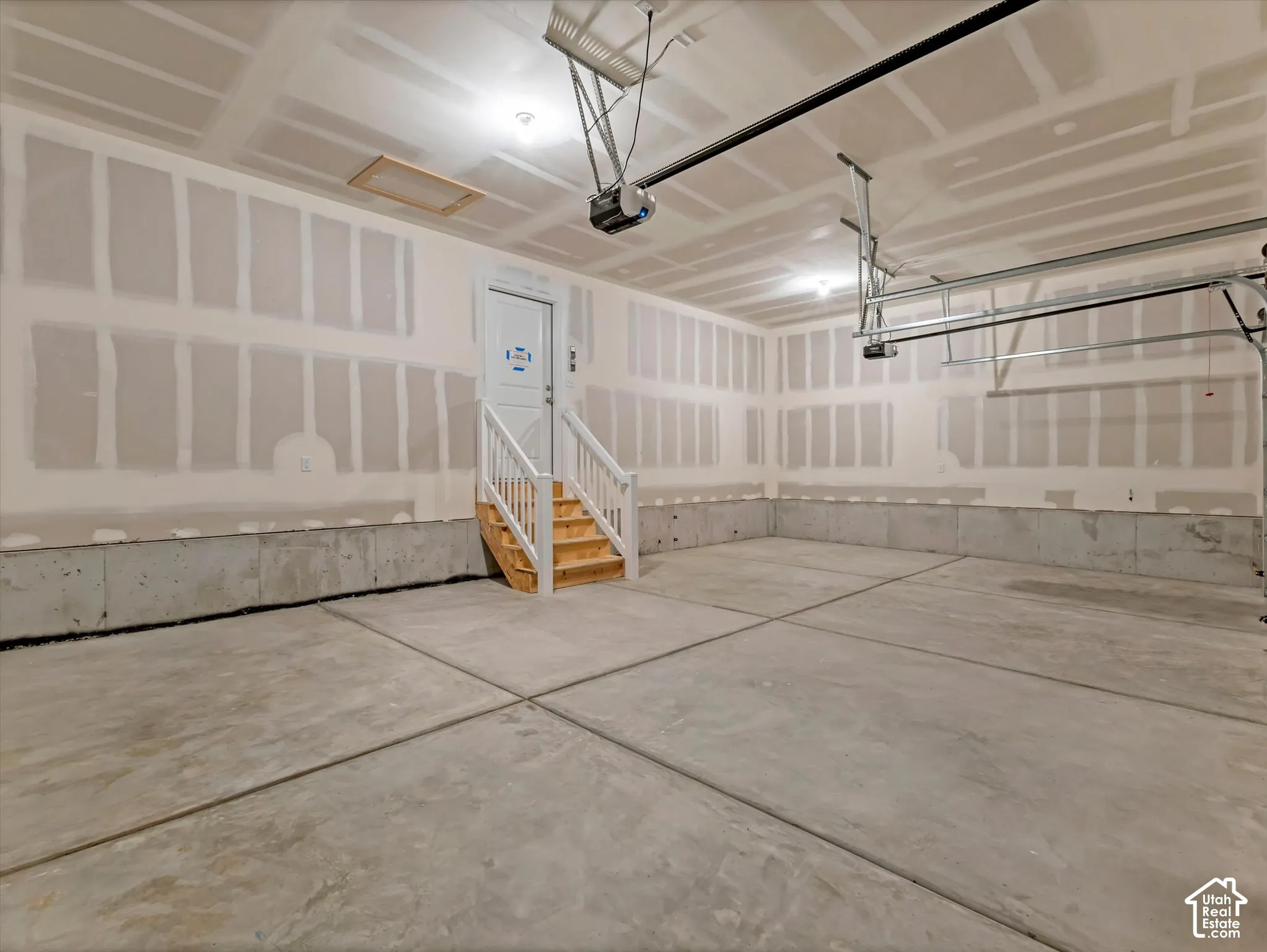 Expansive concrete floor, unfinished drywall, overhead lighting, and built-in door with staircase