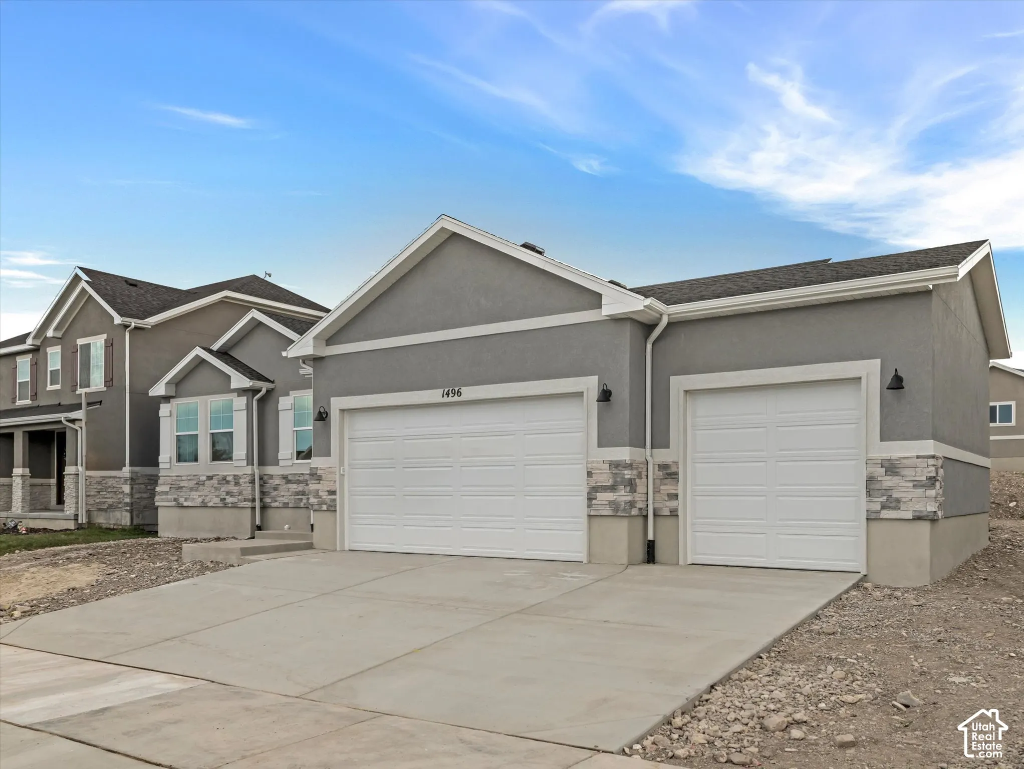 Stucco exterior with stone veneer accents, dual overhead garage doors, and an attached downspout system