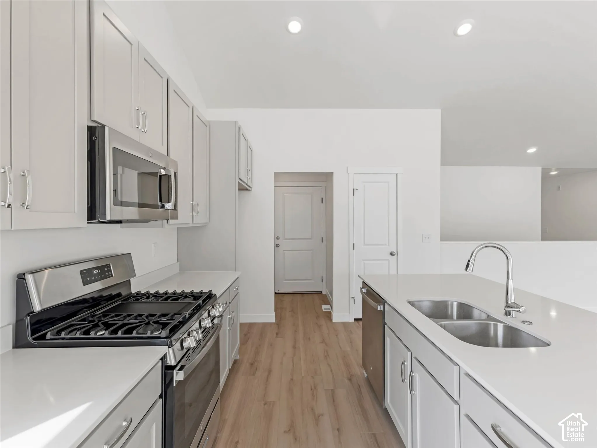 Modern kitchen featuring light cabinetry, stainless steel appliances, wood-finish flooring, recessed lighting, and a kitchen island with an undermount double sink