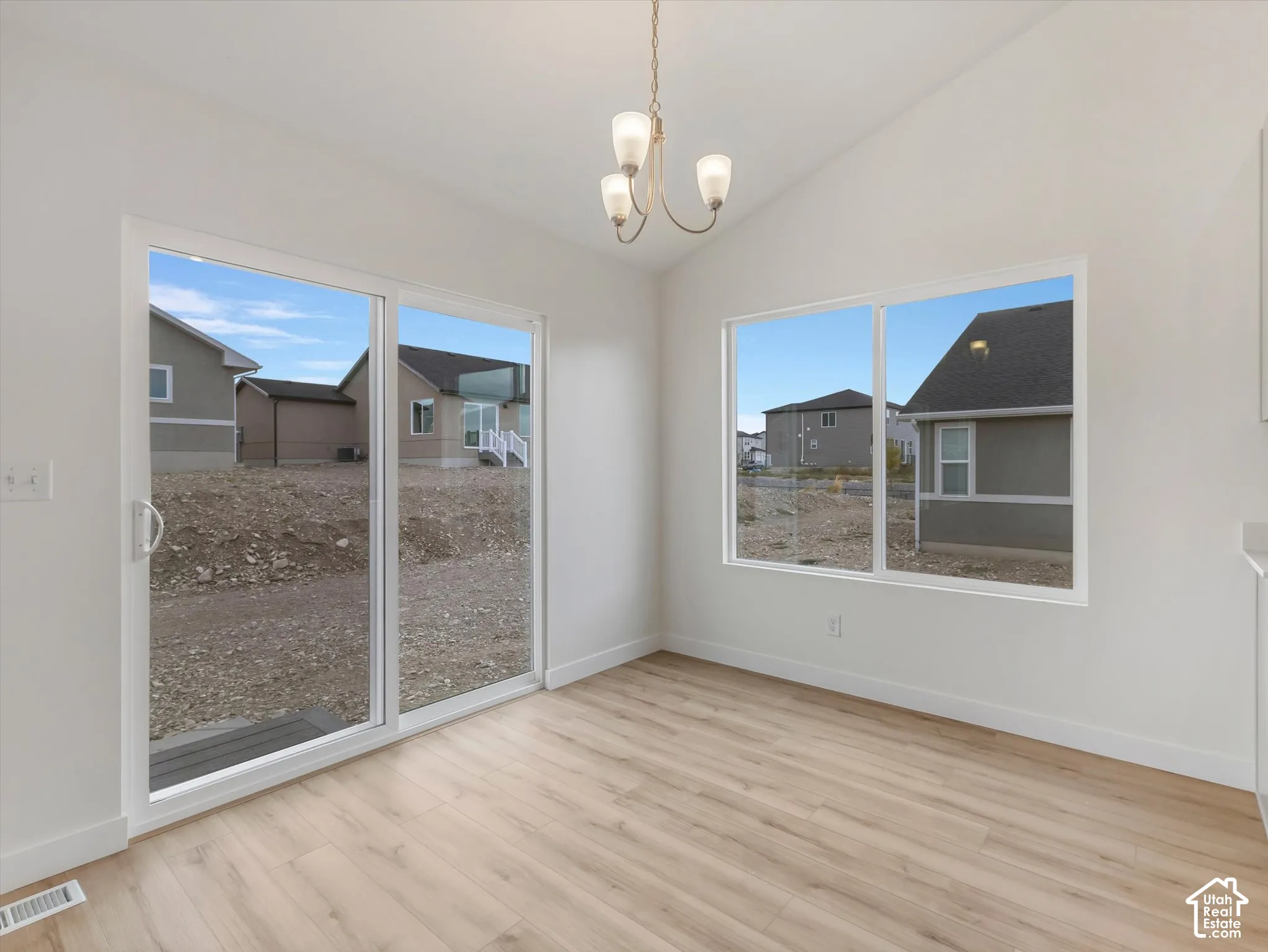 Vaulted ceiling, wood-finish flooring, sliding glass door, white trim, and a three-light chandelier