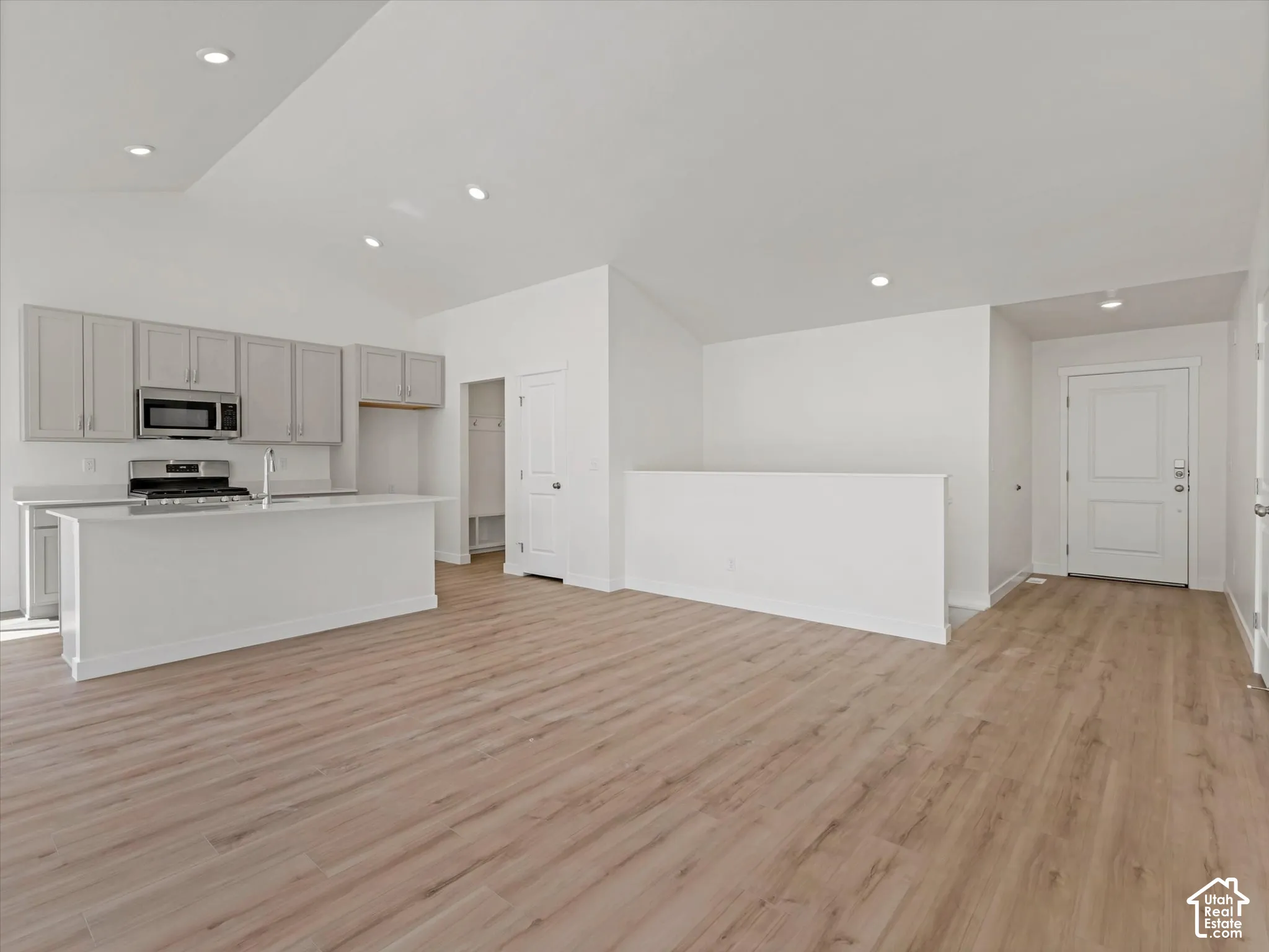 Open-concept living area featuring wood-finish flooring, vaulted ceilings with recessed lighting, and a kitchen with gray cabinetry, a central island, and stainless steel appliances