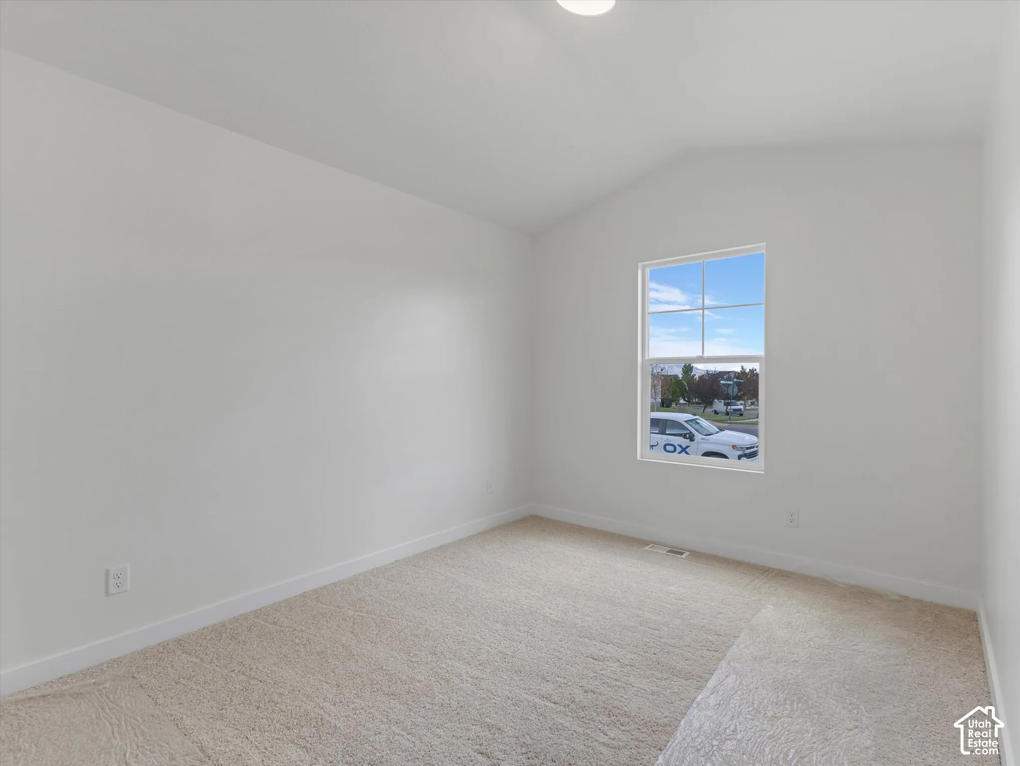 Neutral-toned wall-to-wall carpeting, white painted walls, and a single window with a white frame