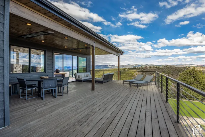 Expansive outdoor deck with a covered portion, wood plank flooring, cable railing, and large window wall