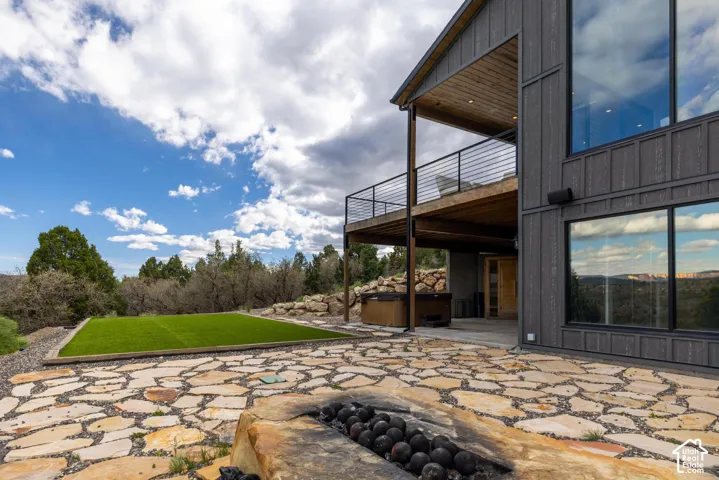 Expansive flagstone patio with a built-in fire pit, artificial turf area, and a hot tub