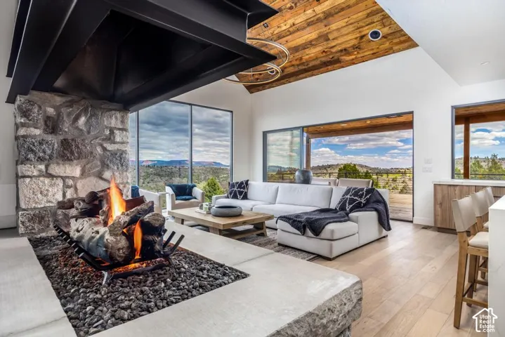 Expansive living space featuring a stone fireplace with a metal hood, wood-finish flooring, a vaulted wood-paneled ceiling, and large sliding glass doors