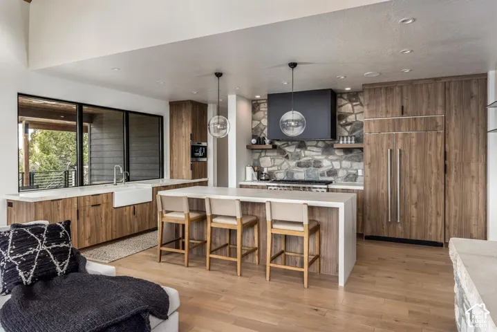 Open-concept kitchen with wood-finish cabinetry, a large center island, stone accent wall, integrated appliances, and a farmhouse sink