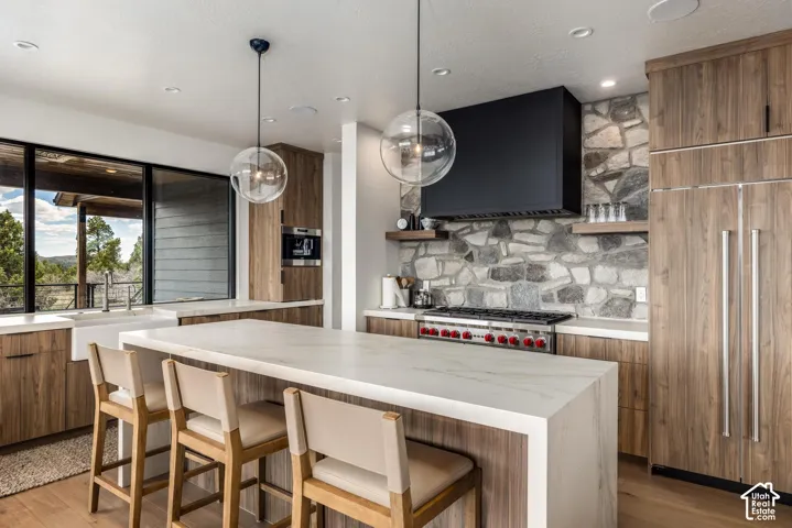 Expansive kitchen featuring a large island with seating, stone-finish backsplash, wood-finish cabinetry, and built-in appliances