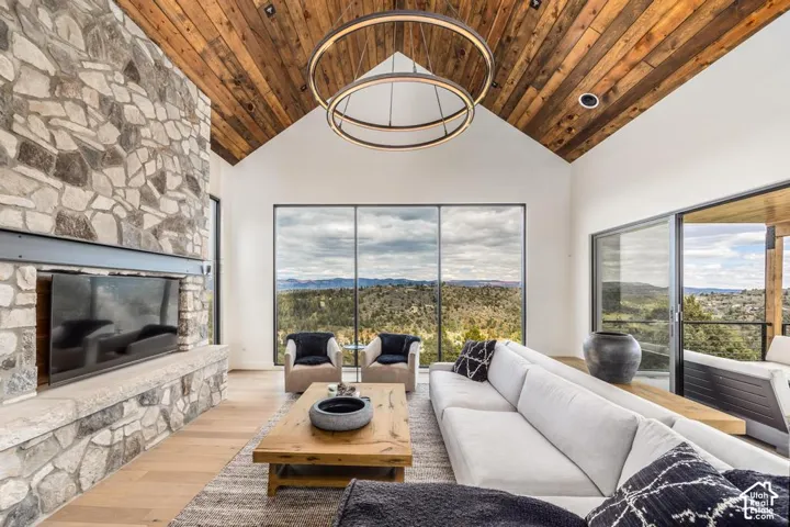Vaulted wood plank ceiling, stone fireplace surround, wide-plank wood-finish flooring, full-height windows, and sliding glass doors to outdoor living space
