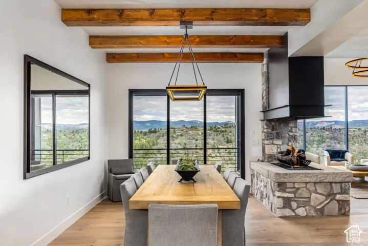 Exposed wood beam ceiling, stone fireplace with hearth, black framed glass doors, and wood-finish flooring