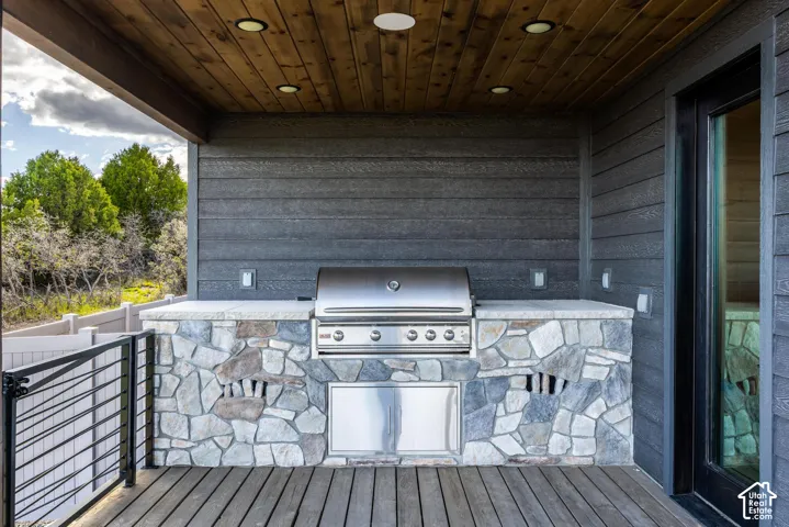 Outdoor kitchen with stone masonry base, stainless steel grill, and wood-finish ceiling