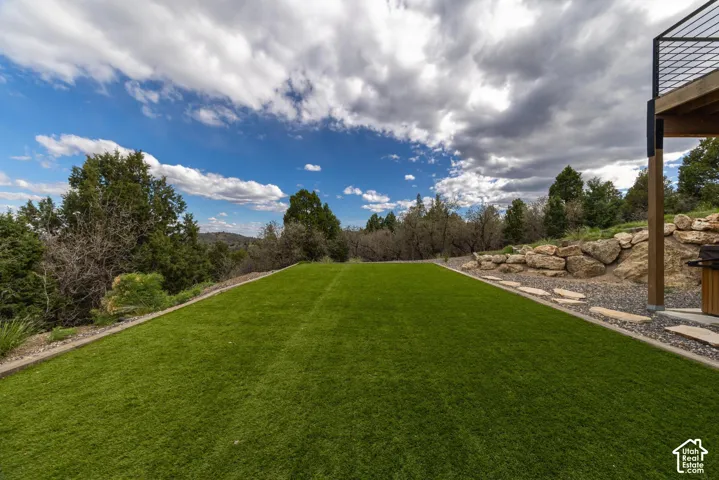 Expansive artificial turf lawn with a stone retaining wall, natural rock landscaping, and mature trees