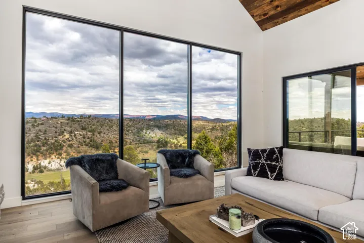 Expansive floor-to-ceiling windows, wood-finish flooring, vaulted ceiling with exposed wood beams, and a sliding glass door