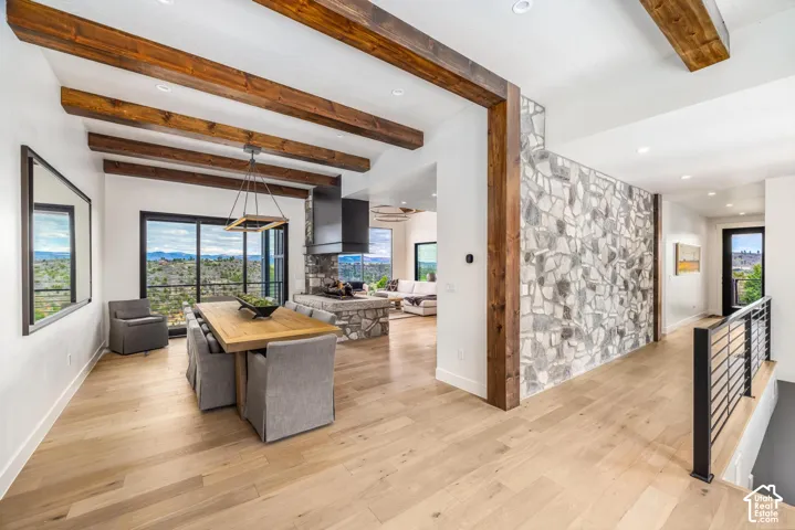 Exposed wood beams, light wood-finish flooring, stone accent wall, black framed sliding glass door, and a metal railing
