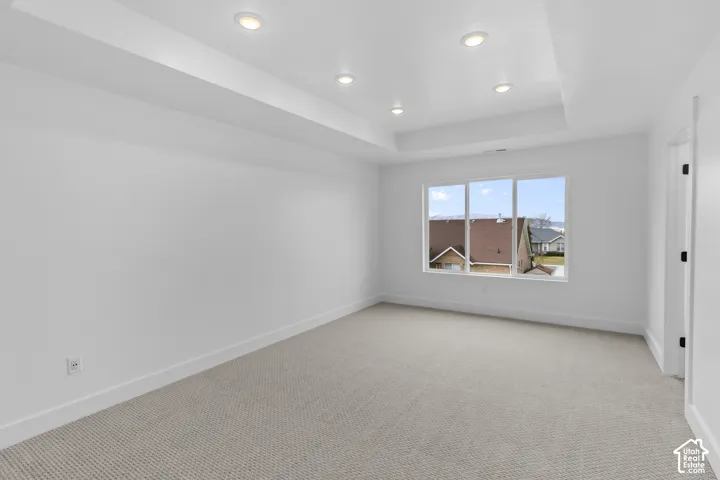 Recessed lighting, tray ceiling, neutral wall color, light-toned carpeting, and a multi-pane window