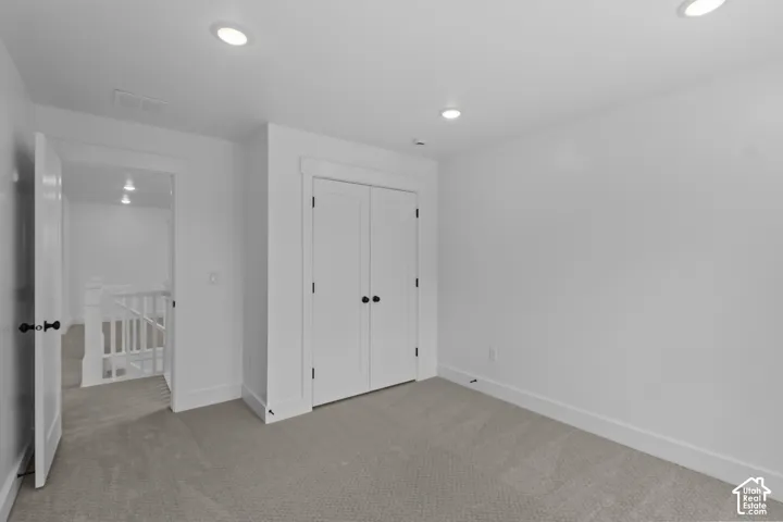 Neutral carpeting, recessed lighting, white walls, and a closet with double doors