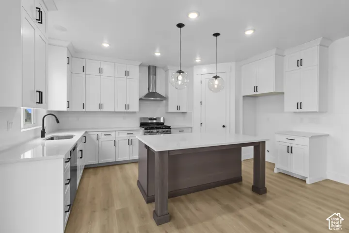Kitchen featuring white shaker cabinetry, light-toned wood-finish flooring, a central island with a contrasting base, and integrated stainless steel appliances