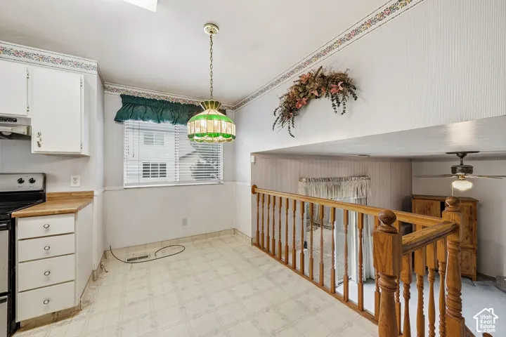 Integrated kitchen area featuring white cabinetry, wood-finish countertops, and a built-in range with an overhead vent