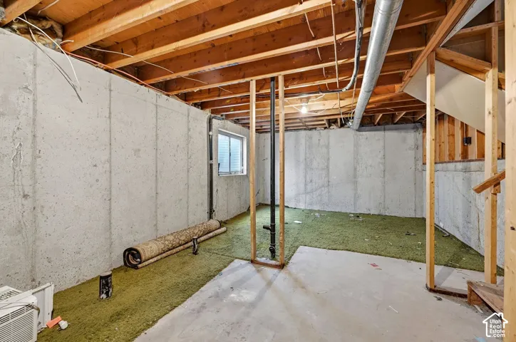 Unfinished basement featuring exposed wood joists, concrete walls, and a window