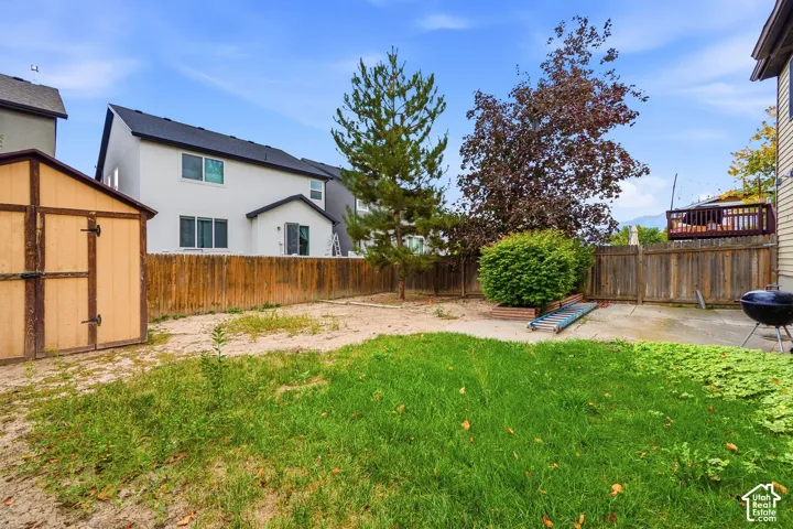 Expansive outdoor space featuring a storage shed, wood fence, mature trees, and a concrete patio area