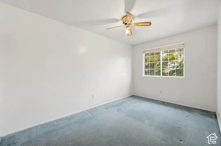 Large window with horizontal blinds, light blue carpeting, and a ceiling fan with integrated lighting
