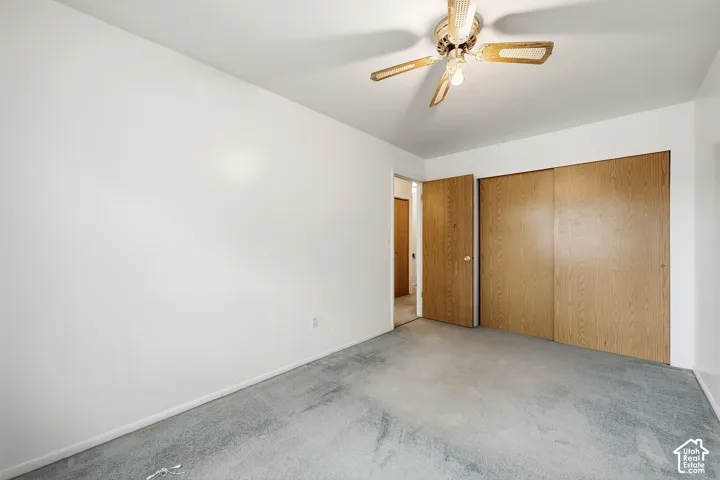 Spacious room with light-colored walls, gray carpeting, and a ceiling fan