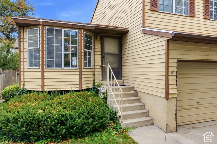 Exterior featuring light-colored horizontal siding, a bay window with multiple panes, a concrete staircase with handrailing, and an attached garage with a horizontal panel door