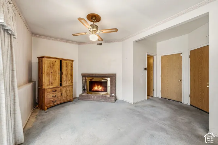 Brick fireplace with a brass firebox, ceiling fan, and carpeted flooring