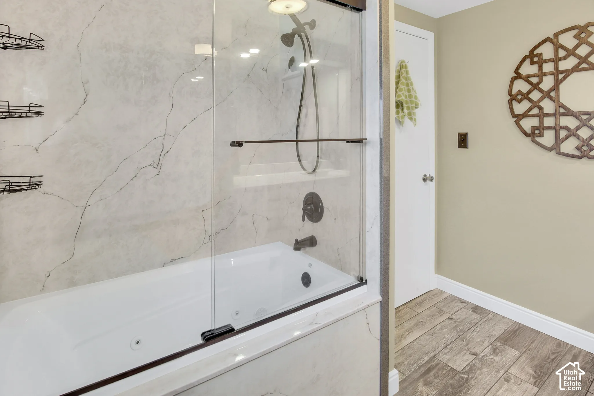White soaking tub with integrated jets, glass shower enclosure, bronze fixtures, and marble-look wall surround
