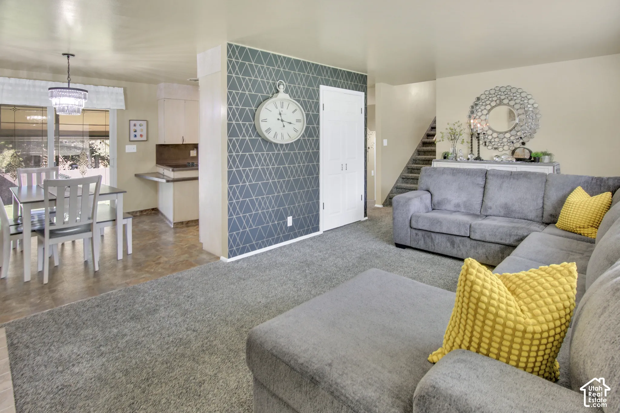Open-concept living space with textured accent wall,  dining area featuring a modern chandelier, and a kitchen pass-through