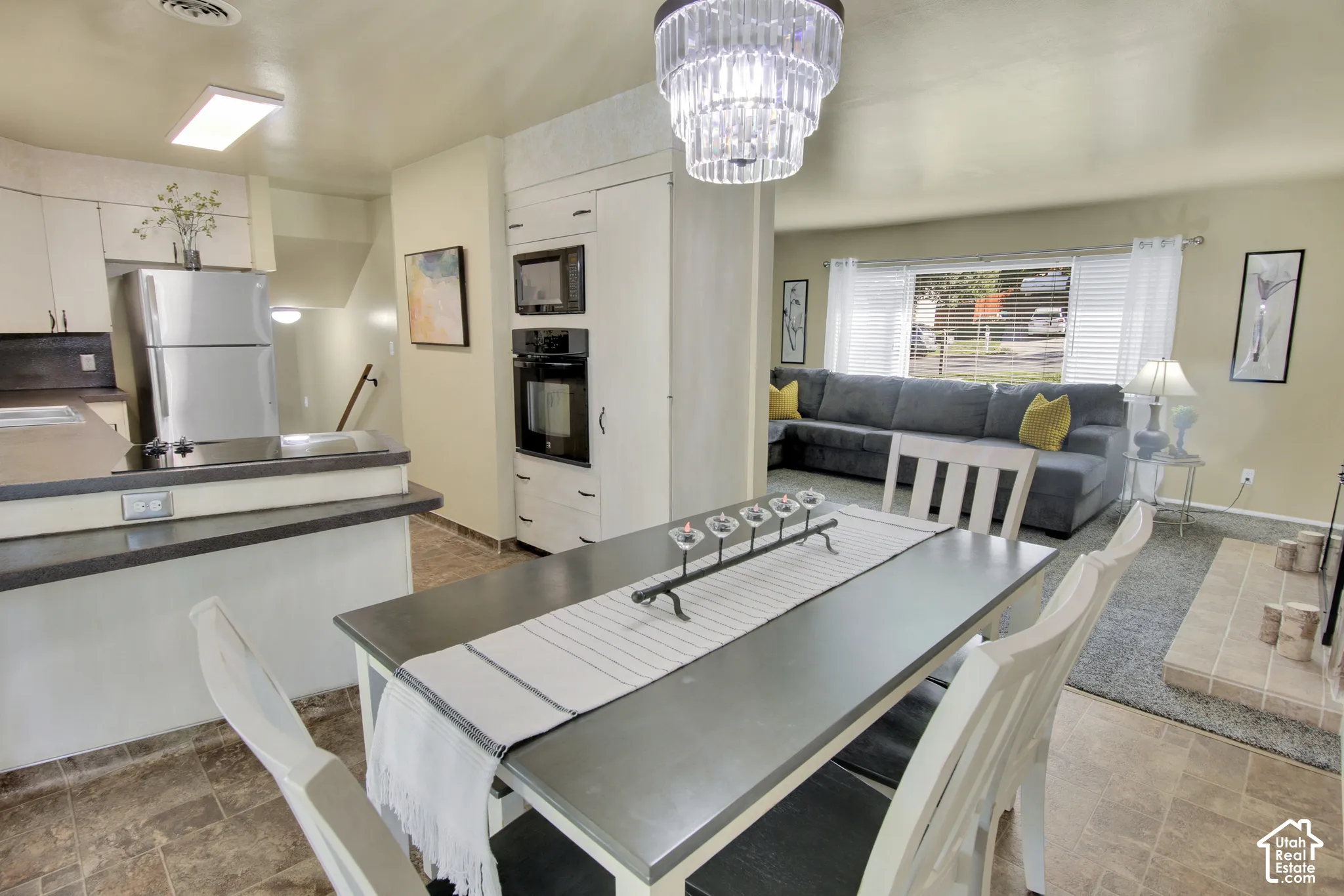 Dining area with a tiered crystal chandelier, an integrated kitchen with built-in appliances. Living room in the background