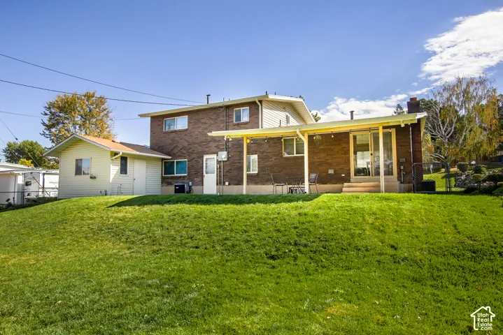 Expansive grass-covered lawn with a two-story brick exterior, attached covered patio, storage shed, and mature landscaping