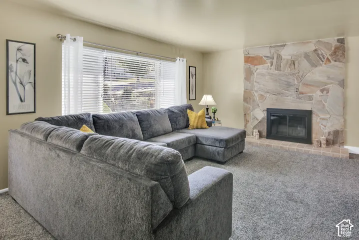 Stone-clad fireplace with a hearth, wall-to-wall carpeting, and large window with blinds