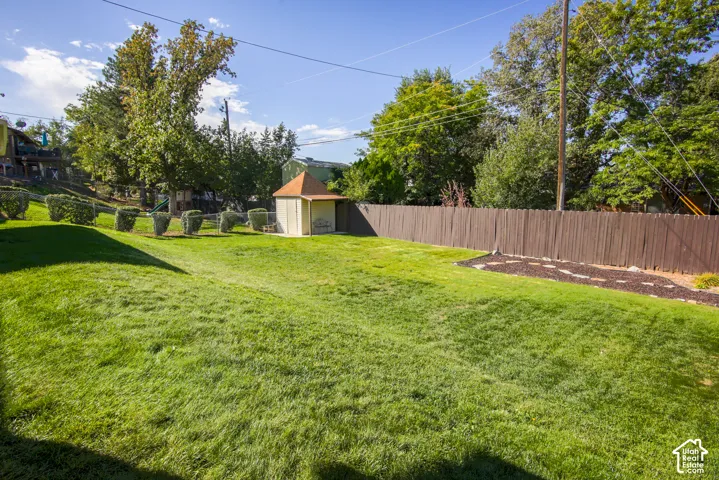 Expansive lawn area with a privacy fence, mature trees, manicured shrubs, and a storage shed