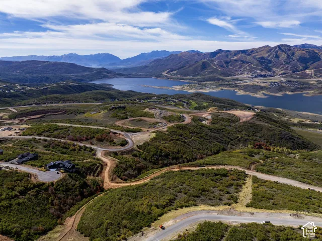 Expansive mountainous terrain featuring a large body of water, distant mountains, paved roads, and scattered residential structures