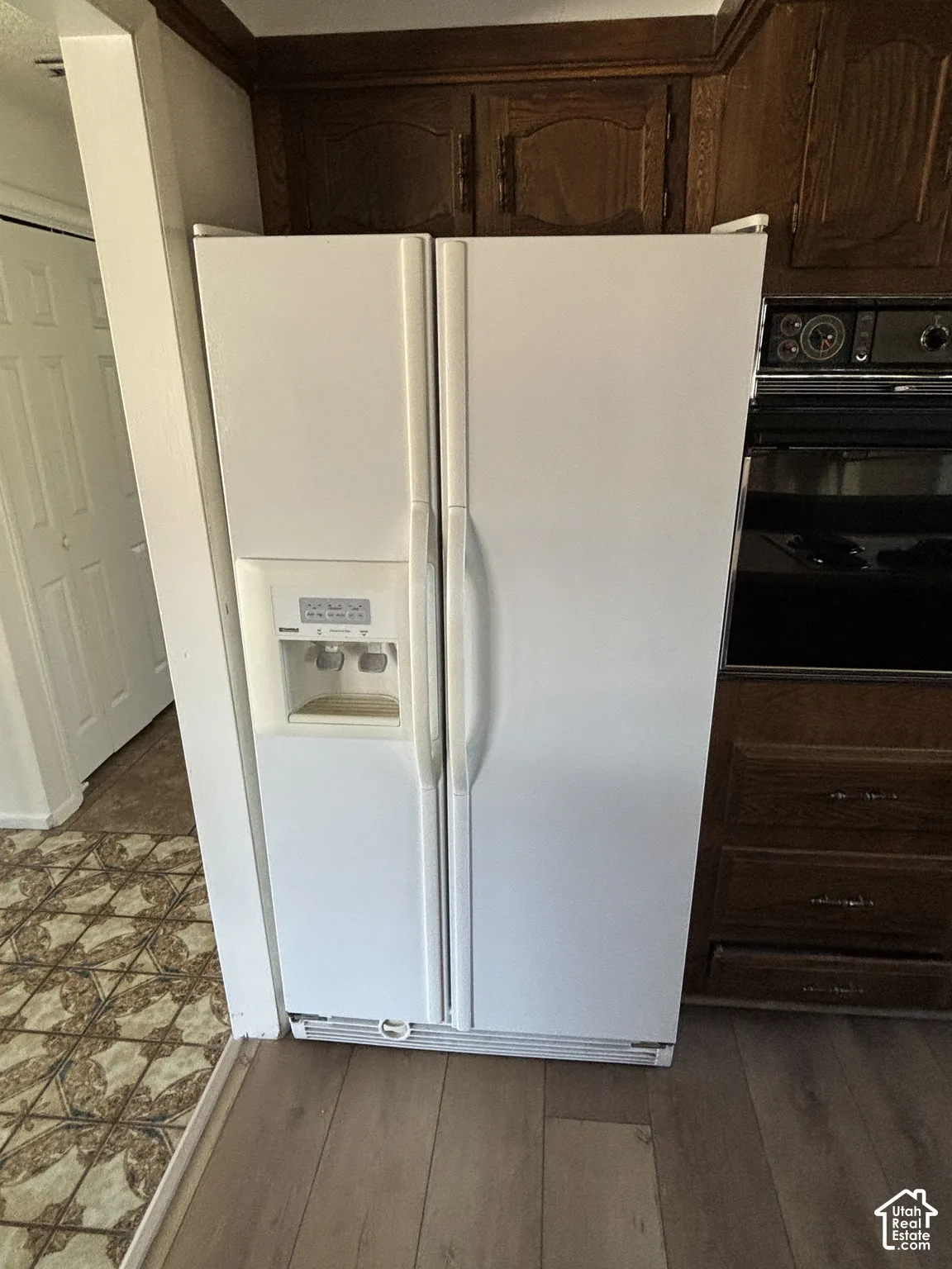 White side-by-side refrigerator with an integrated ice and water dispenser, dark wood-finish cabinetry, and wood-finish flooring