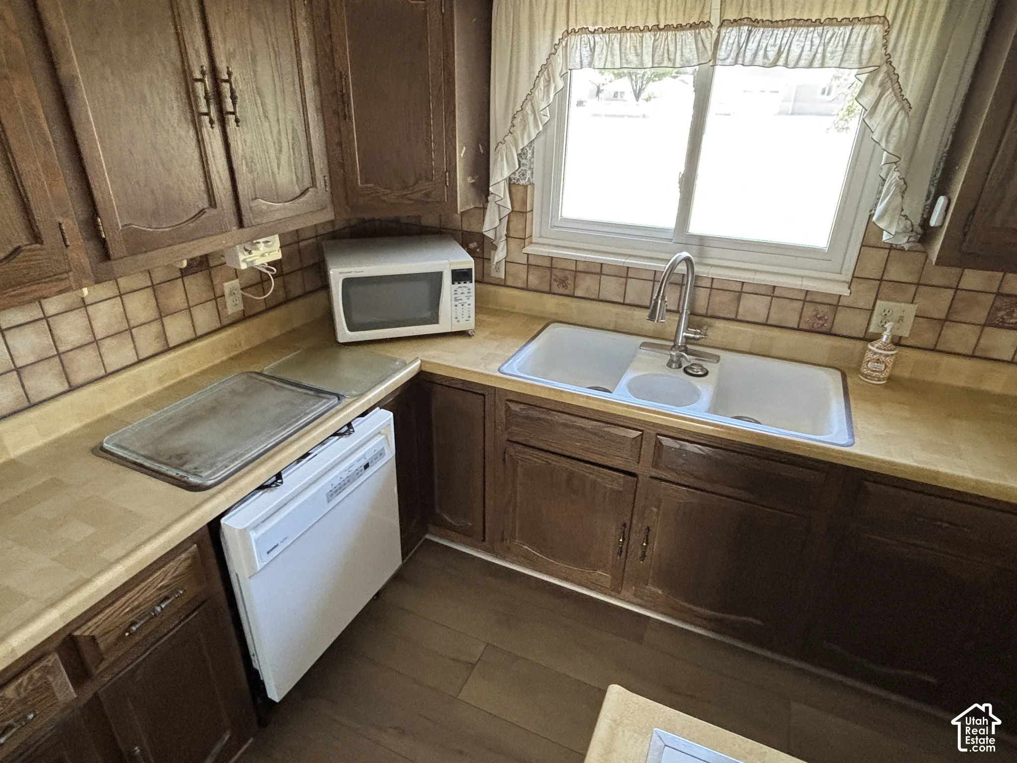 Kitchen featuring wood-finish cabinetry, a double basin sink, and a built-in dishwasher