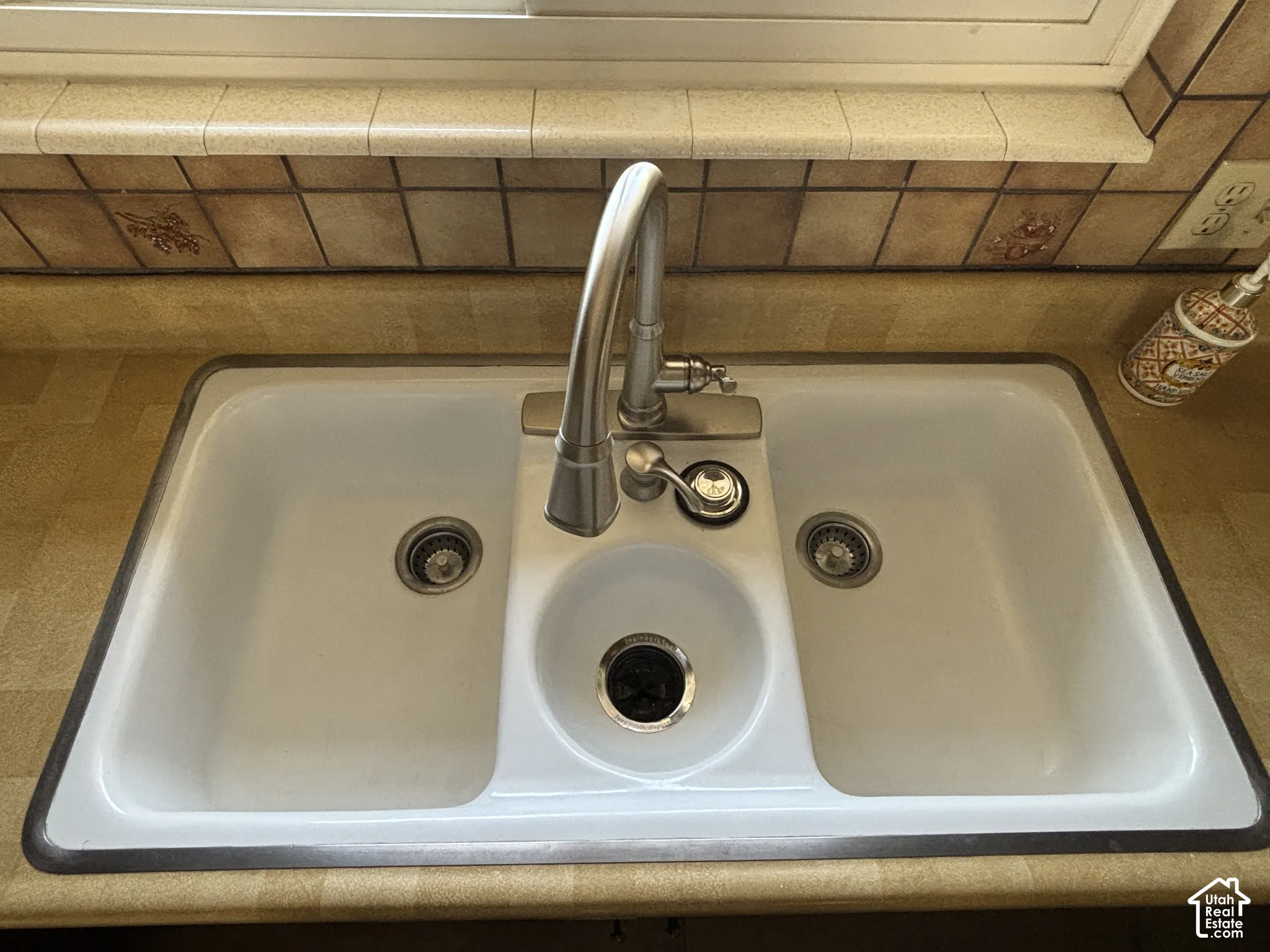 Dual-basin white sink with integrated disposal and faucet, set into a light-toned countertop, and complemented by a tiled backsplash