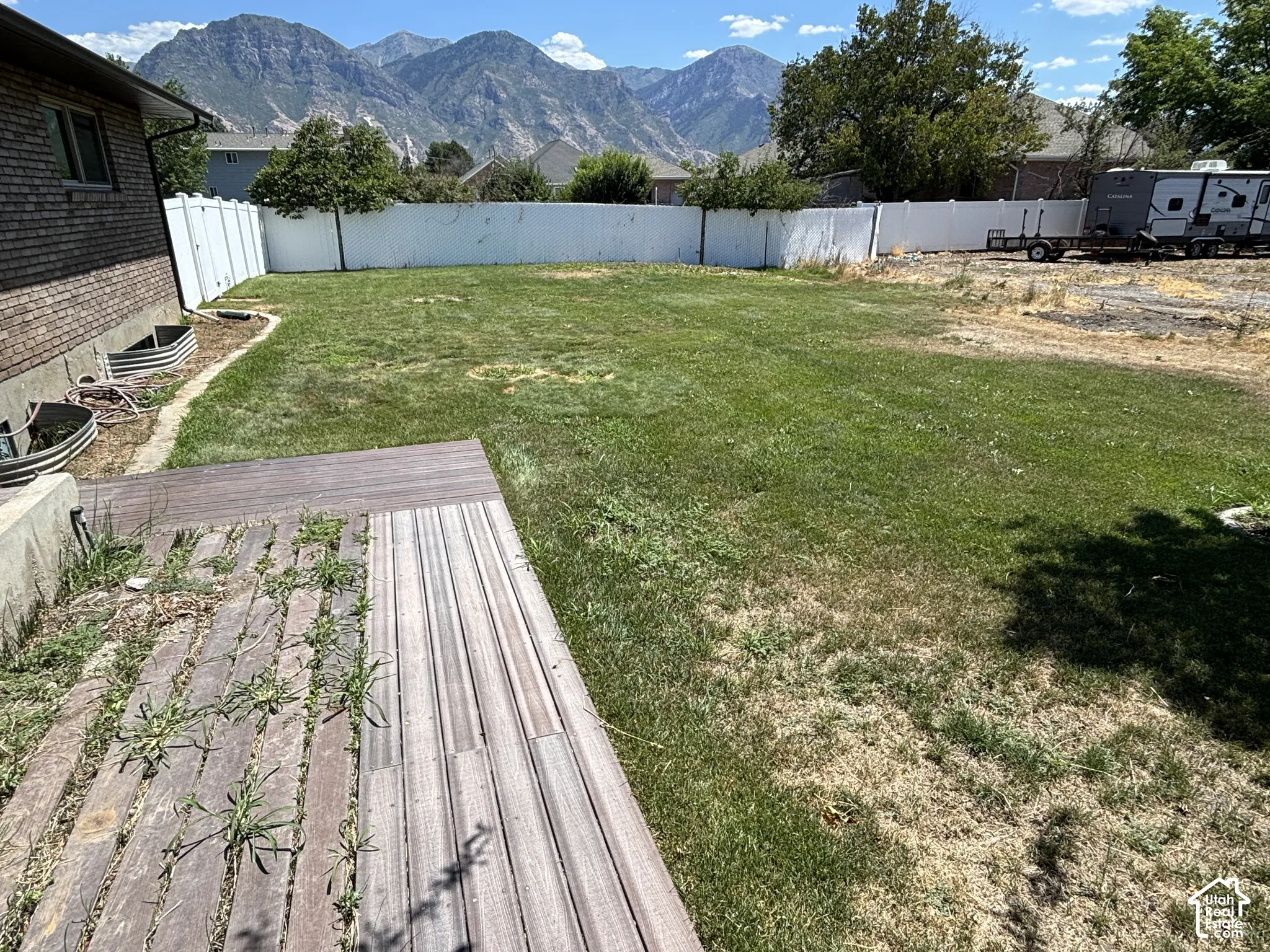Expansive backyard featuring a large grass area, wood-finish decking, and a surrounding white privacy fence