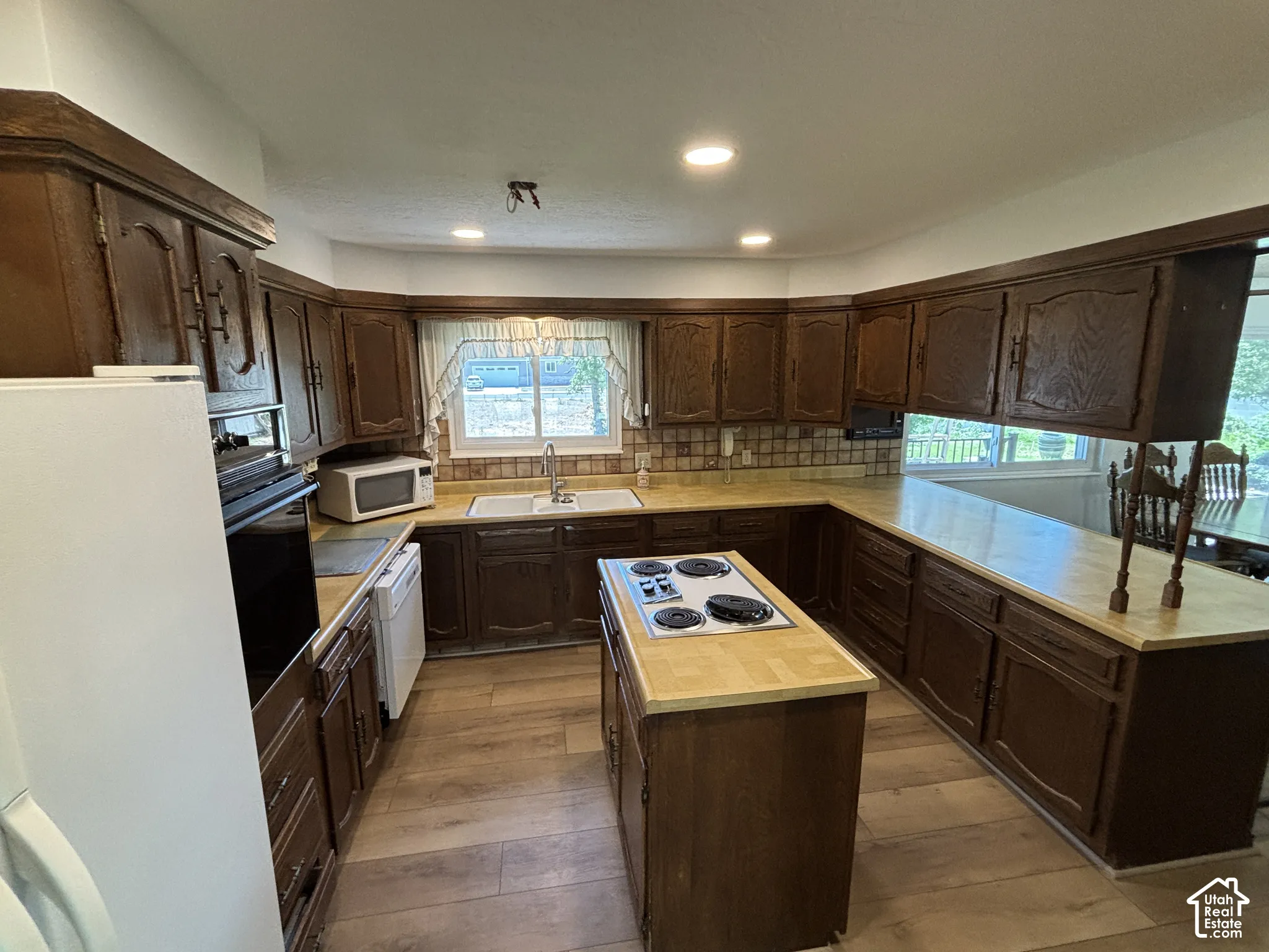 U-shaped kitchen layout featuring wood-finish cabinetry, a built-in wall oven, a center island with a cooktop, and wood-finish countertops
