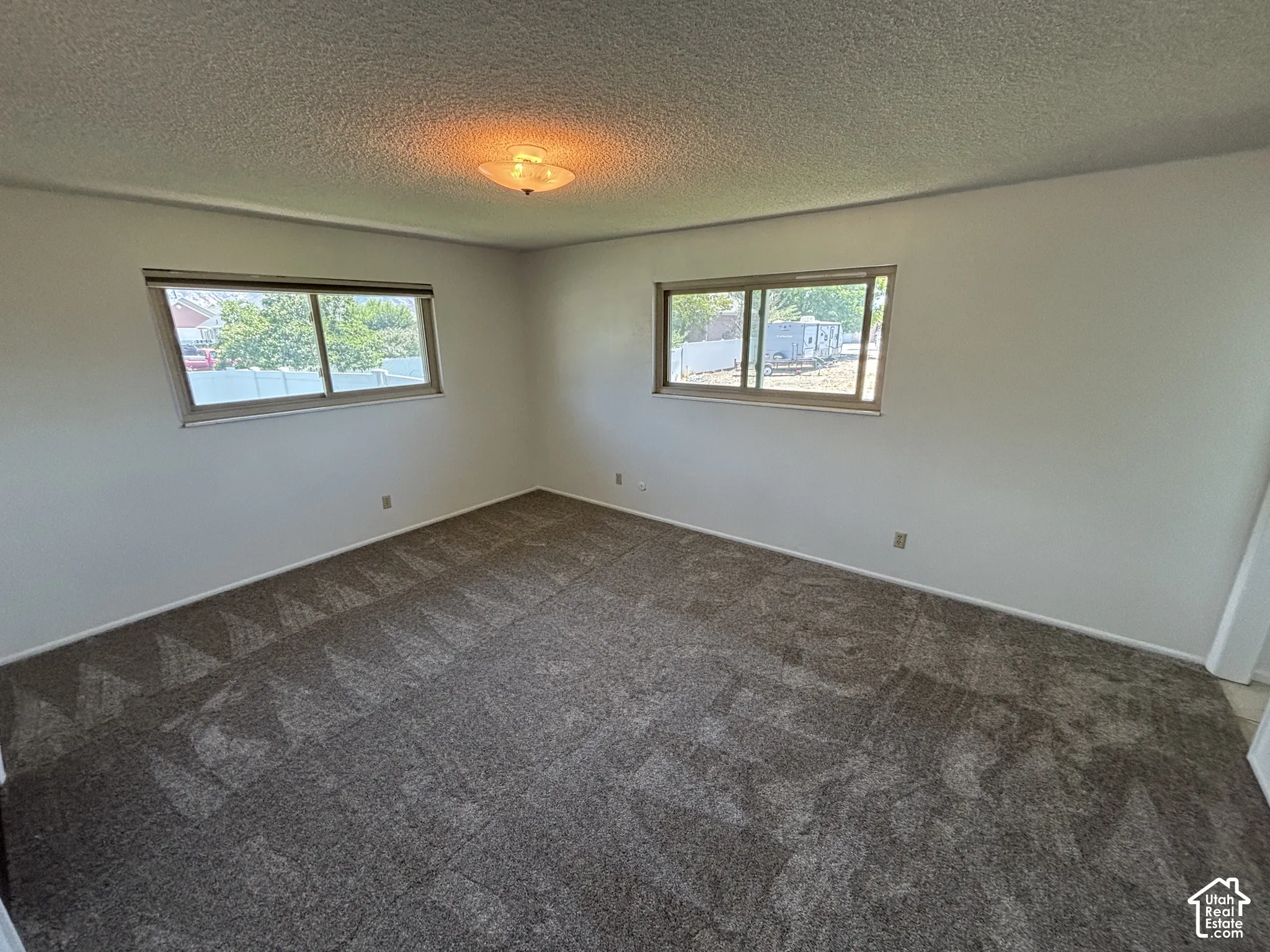 Room featuring two windows, neutral wall paint, textured ceiling, and patterned carpet flooring