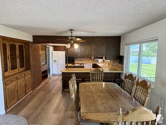 Wood-finish flooring, built-in wooden cabinetry, ceiling fan with light fixture, kitchen with U-shaped counter, and a large window