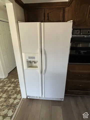 White side-by-side refrigerator with an integrated ice and water dispenser, dark wood-finish cabinetry, and wood-finish flooring