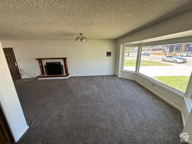 Spacious living area featuring a bay window, a built-in fireplace with a wood-finish mantel, and textured carpeting