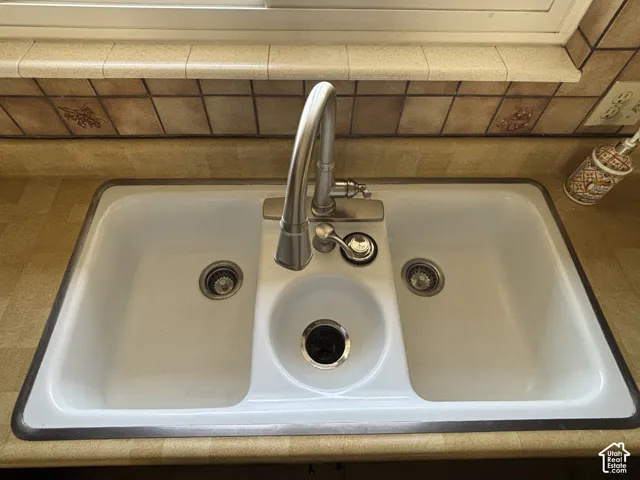Dual-basin white sink with integrated disposal and faucet, set into a light-toned countertop, and complemented by a tiled backsplash