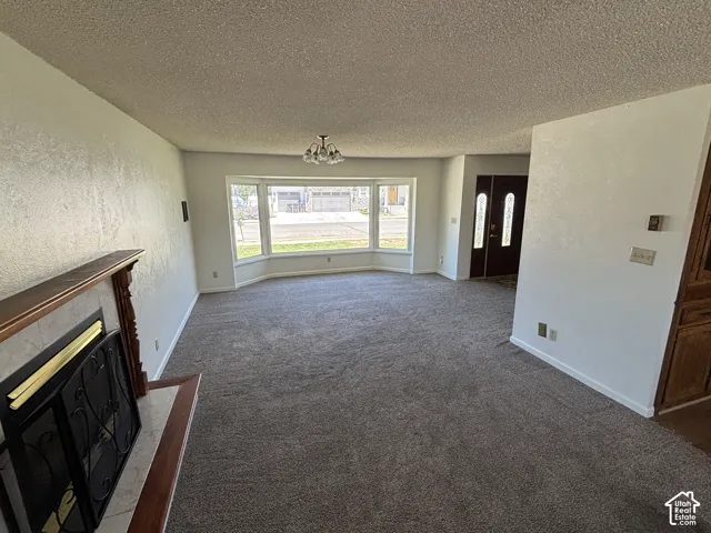 Spacious living area featuring bay windows, textured walls, a built-in fireplace with a mantel, and a dark wood entry door